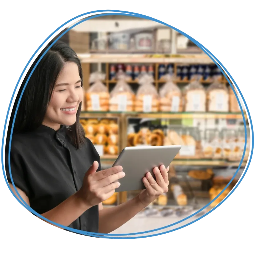 A shop owner smiling while using a tablet in her bakery