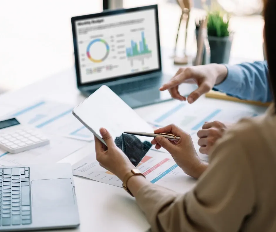 Two people reviewing charts on a laptop and paper reports